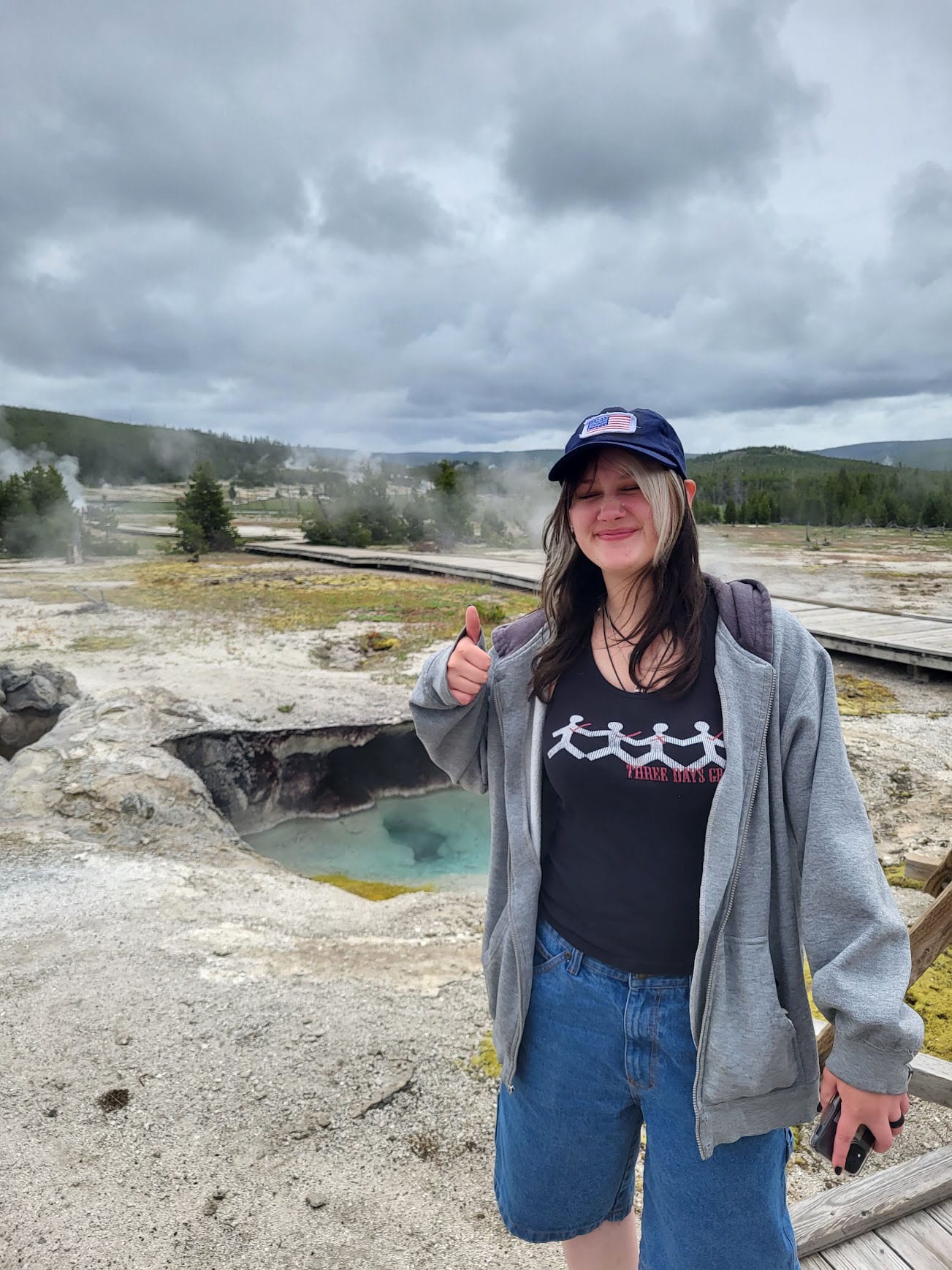 FIXED-yellowstone Girl standing in front of a natural geyser from Yellowstone, pointing at it.
